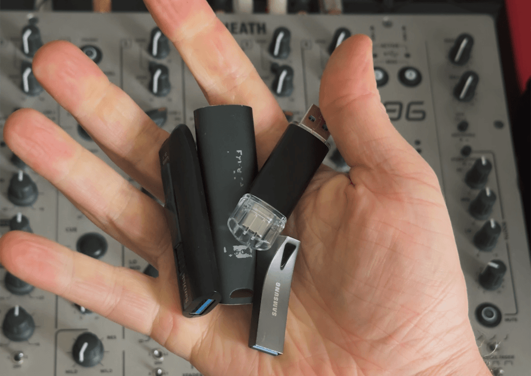 A hand holding four different USB sticks above a XONE 96 mixer